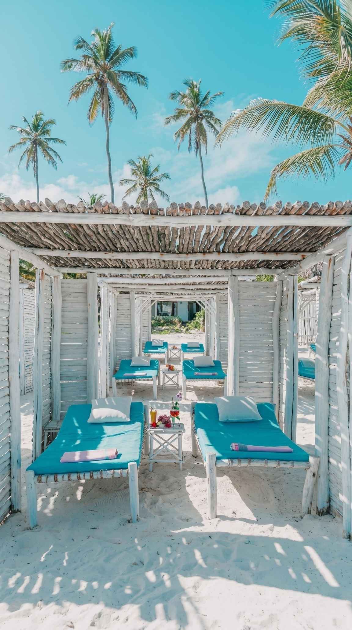 The private beach club at Exploreans Watamu — palms, makuti gazebos, and the open Indian Ocean.